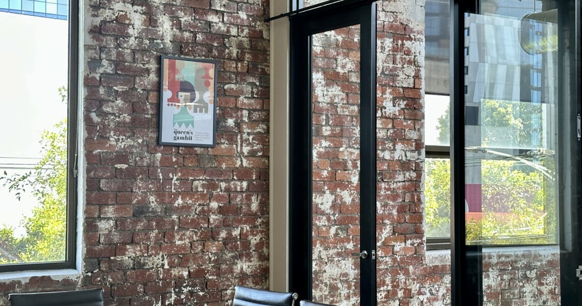 Framed Queen’s Gambit artwork on exposed brick wall with sunlight filtering into the boardroom (called The Queen's Gambit) a meeting room at ko&co workhub South Melbourne. A coworking space.
