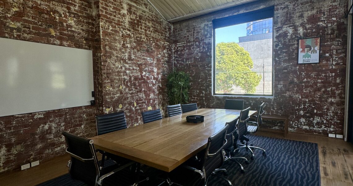 Large boardroom (called The Queen's Gambit) with exposed brick walls, a timber meeting table, and modern office chairs at ko&co workhub South Melbourne