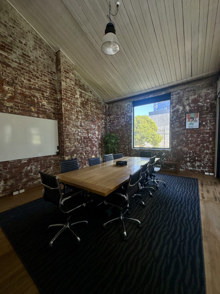 Large boardroom (called The Queen's Gambit) with exposed brick walls, a timber meeting table, and modern office chairs at ko&co workhub South Melbourne