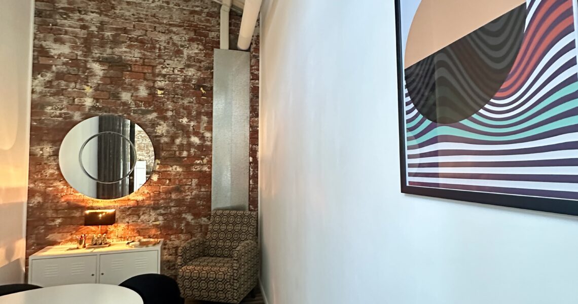 Framed “The Looking Glass” artwork in styled meeting room with exposed brick wall and round mirror. ko&co workhub South Melbourne