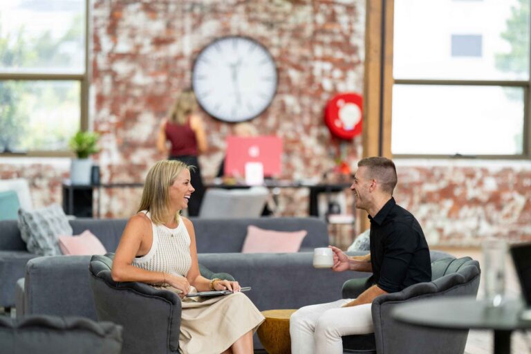 Two coworkers laughing and chatting in the lounge area at ko&co workhub, surrounded by plush seating and exposed brick walls. Coworking in the heart of South Melbourne