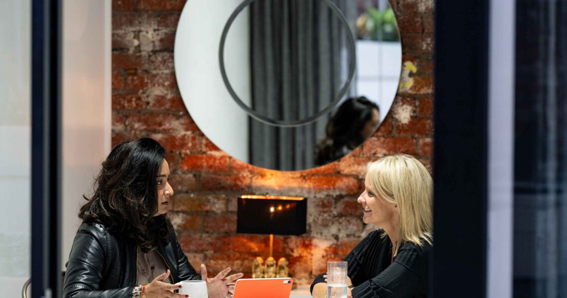 Two women having a collaborative meeting inside The Looking Glass room at ko&co workhub, with warm lighting and exposed brick wall. South Melbourne coworking space